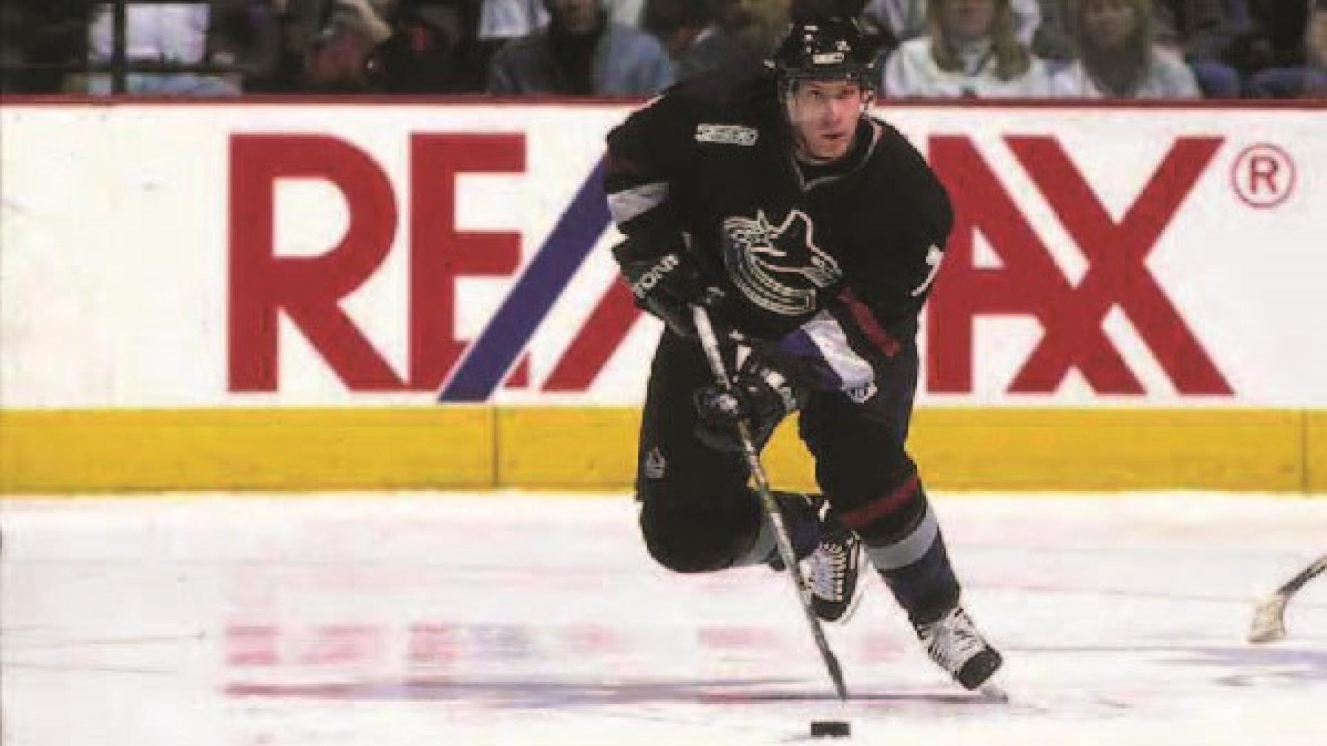 Brendan Morrison bends down to get his stick on the ice in a game of hockey.